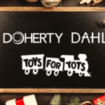 Doherty, DAHL & Toys for Tots white logos on chalkboard sign surrounded by holiday wrapping paper