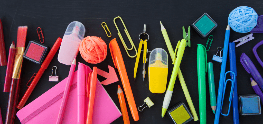 a rainbow of school supplies laid out from red to purple on a black background.
