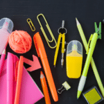 a rainbow of school supplies laid out from red to purple on a black background.