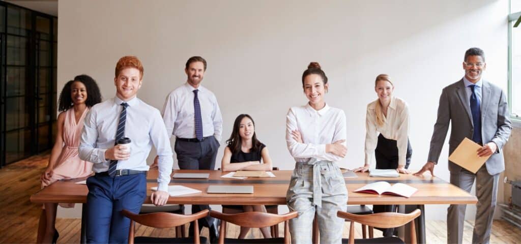 A group of professionals standing around a table and smiling at camera in an office setting